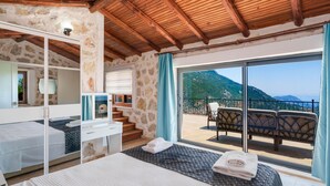 A bedroom with a wooden ceiling, stone walls, a balcony with chairs, and a view of mountains. - Villa Elvin in İslamlar Köyü (İslamlar Köyü)