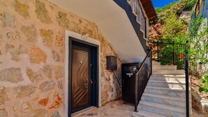 A stone building with a wooden door, a staircase with a black railing, and a view of a hillside. - Villa Elvin in İslamlar Köyü (İslamlar Köyü)