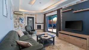 A modern living room with a sofa, armchair, and a flat-screen TV mounted on the wall. - Villa Elvin in İslamlar Köyü (İslamlar Köyü)