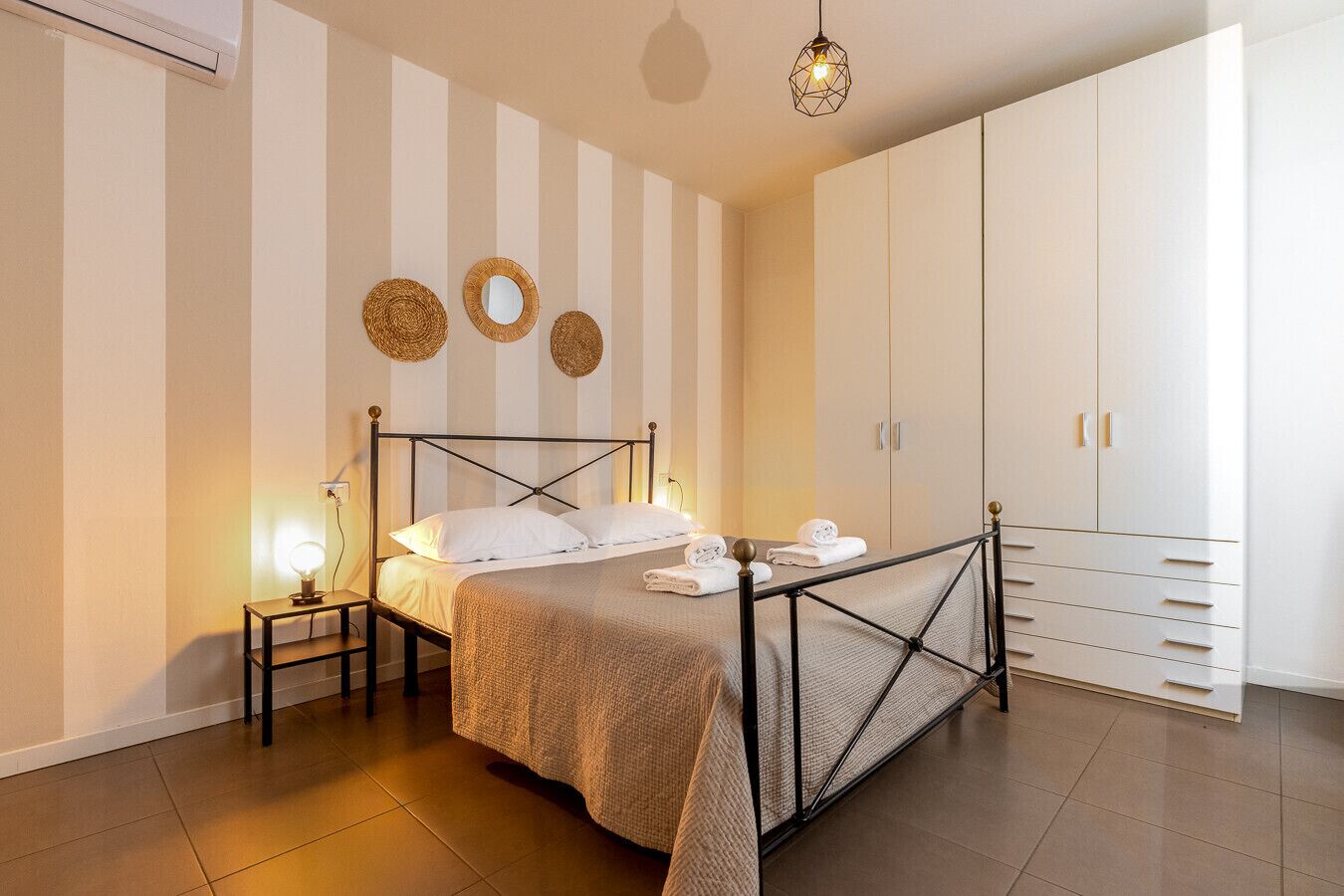 A bedroom with a bed, bedside lamps, a wardrobe, and decorative wall mirrors.