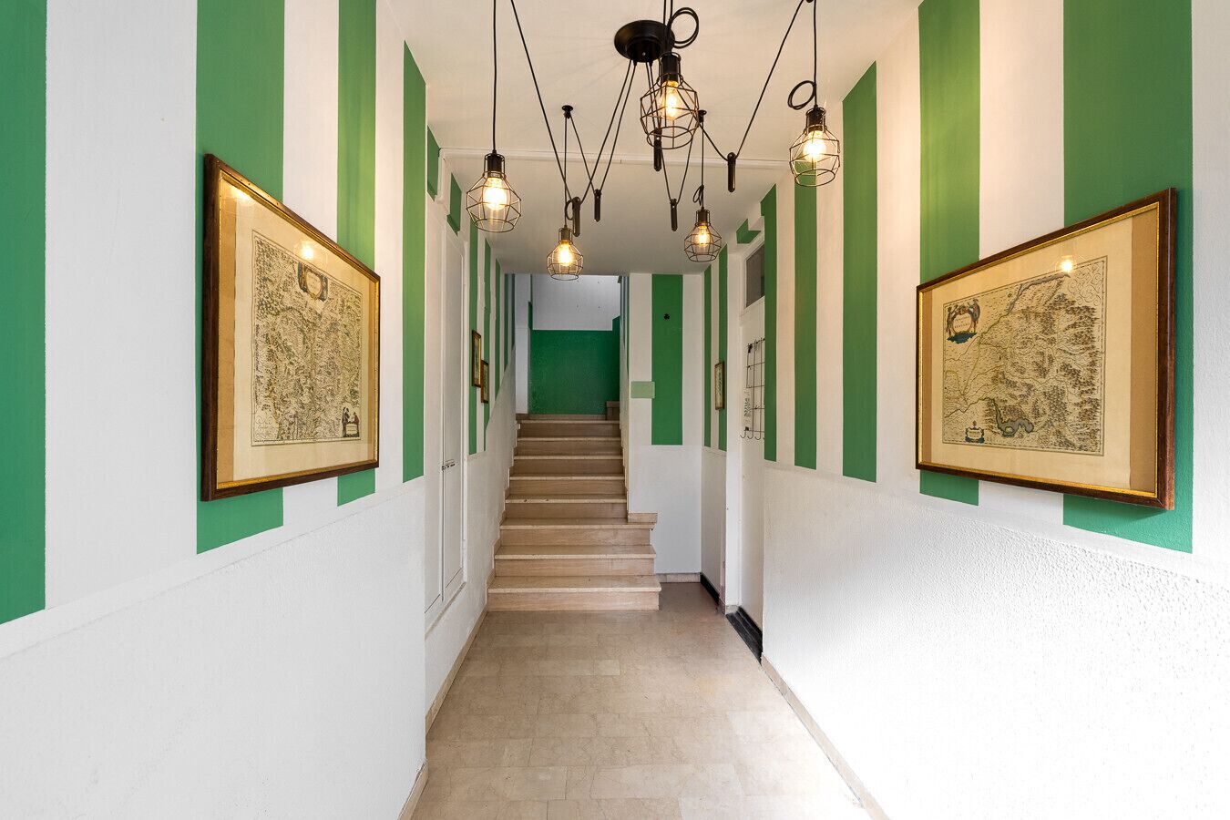 A hallway with green and white walls, framed pictures, a staircase, and hanging light fixtures.