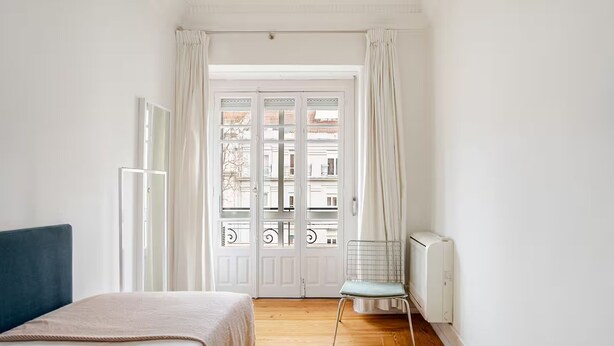 Et værelse med en seng, en stol, en radiator og en dør med udsigt til en balkon.