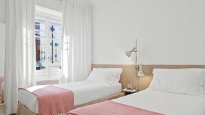 Et hotelværelse med to senge, et vindue med gardiner, en sengebordlampe og trægulv.