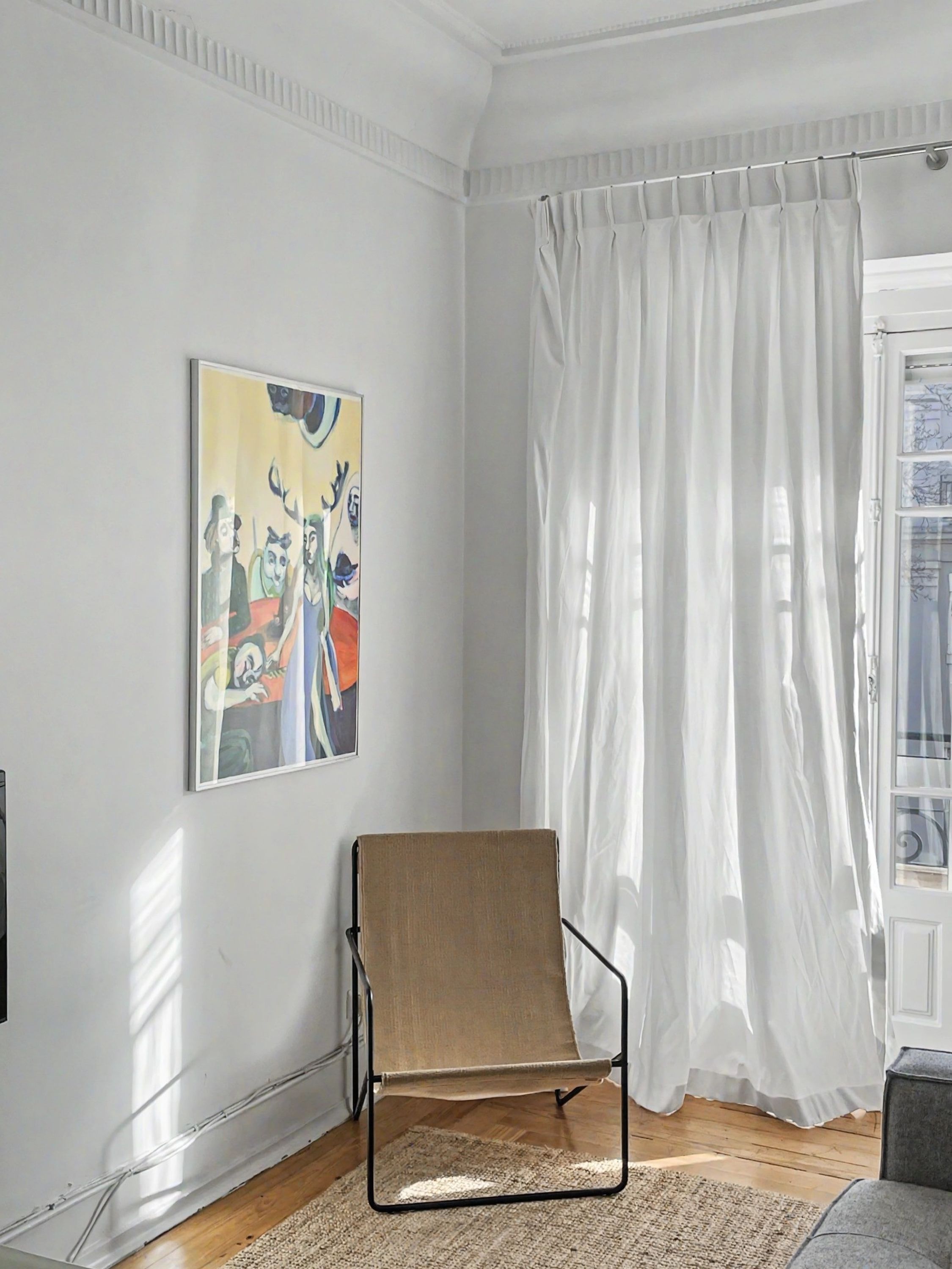 Una habitación con una silla, un cuadro, una ventana con cortinas y una puerta.