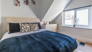 Ein Schlafzimmer mit Bett, Fenster, Nachttisch und Wandbildern.