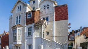 Ein mehrstöckiges Gebäude mit weißer Fassade, roten Backstein-Akzenten und einem Erkerfenster mit Buntglas.