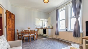 Eine moderne Küche mit weißen Schränken, ein Essbereich mit Holzsesseln und ein großes Fenster mit Vorhängen.