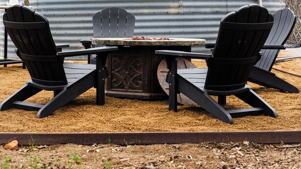 A large cylindrical metal building with a small window and an attached electrical box. In front, there is a table with two chairs and a fire pit. - The Silo On 16 (Graham)