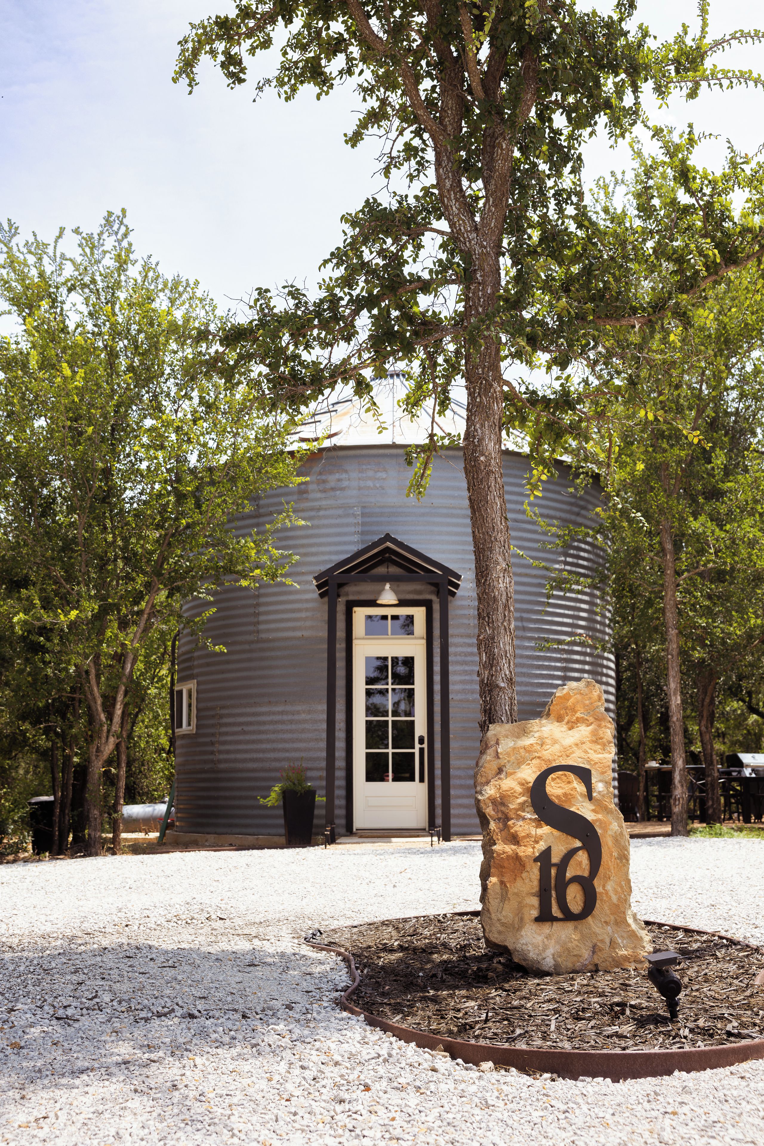 A building with a dark exterior, a white door, and a large stone with the number '16' in front.
