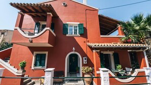 A two-story building with a red facade, green shutters, and a balcony. - Standard Studio near the beach (Agios Gordios)