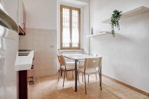 Eine Küche mit Fenster, weißen Schränken, einer weißen Arbeitsplatte und einem Esstisch mit Stühlen.