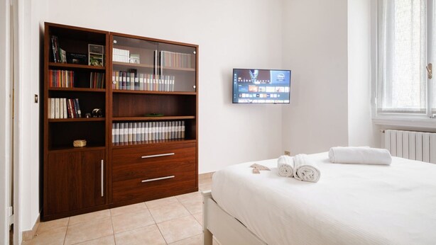 A bedroom with a bed, a wooden bookshelf, a television, and a window. - The Light Flat Bonghi is a bright and welcoming apartment just steps from Bocconi University, ideal for seating up to 6 people.It has two bedrooms and a living room with a sofa bed, perfect for relaxing moments after a day in the city.The rooms are well- (Milan)