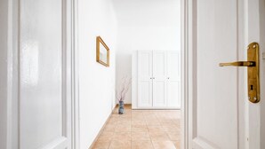 A hallway with white walls, a tiled floor, a door with a brass handle, and a white wardrobe in the background. - The Light Flat Bonghi is a bright and welcoming apartment just steps from Bocconi University, ideal for seating up to 6 people.It has two bedrooms and a living room with a sofa bed, perfect for relaxing moments after a day in the city.The rooms are well- (Milan)