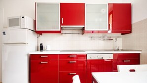 A kitchen with red cabinets, a white refrigerator, and a white countertop. - The Light Flat Bonghi is a bright and welcoming apartment just steps from Bocconi University, ideal for seating up to 6 people.It has two bedrooms and a living room with a sofa bed, perfect for relaxing moments after a day in the city.The rooms are well- (Milan)