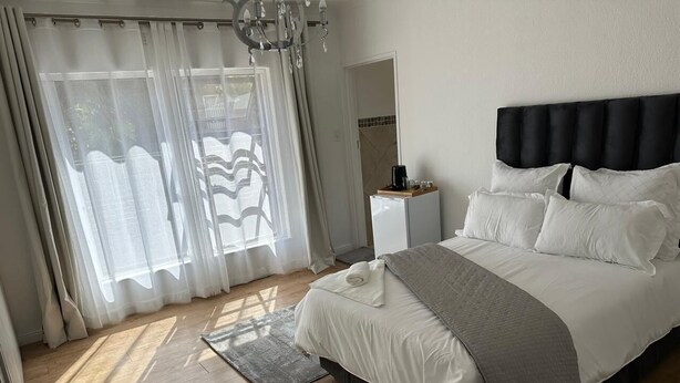 A bedroom with a bed, a nightstand, a window with curtains, and a wooden floor. - Plattekloof guest house (Cape Town)