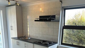 A modern kitchen with white cabinets, a black stove, and a window with a view of greenery. - Plattekloof guest house (Cape Town)