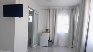 A hotel room with a bed, a TV mounted on the wall, a small kitchenette, and a sliding glass door leading to a balcony. - Plattekloof guest house (Cape Town)