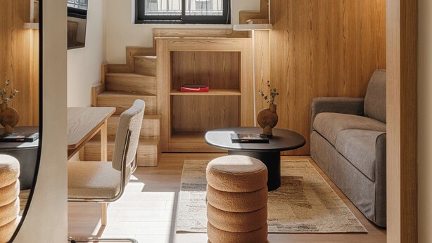 A modern living room with a wooden staircase, a sofa, a coffee table, and a TV mounted on the wall. - Leon II by Zoia Living (Piraeus)