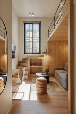 Una sala de estar moderna con una escalera de madera, un sofá, una mesa de centro y un televisor montado en la pared.