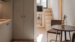 A modern kitchen with a built-in oven, a dining area with a round table and chairs, and a staircase leading to an upper floor. - Leon II by Zoia Living (Piraeus)