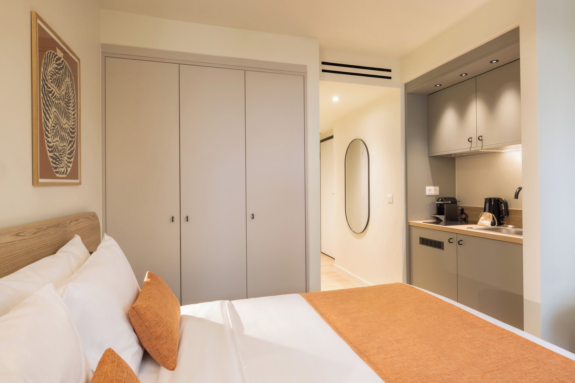 A hotel room with a bed, a wardrobe, a mirror, and a kitchenette.