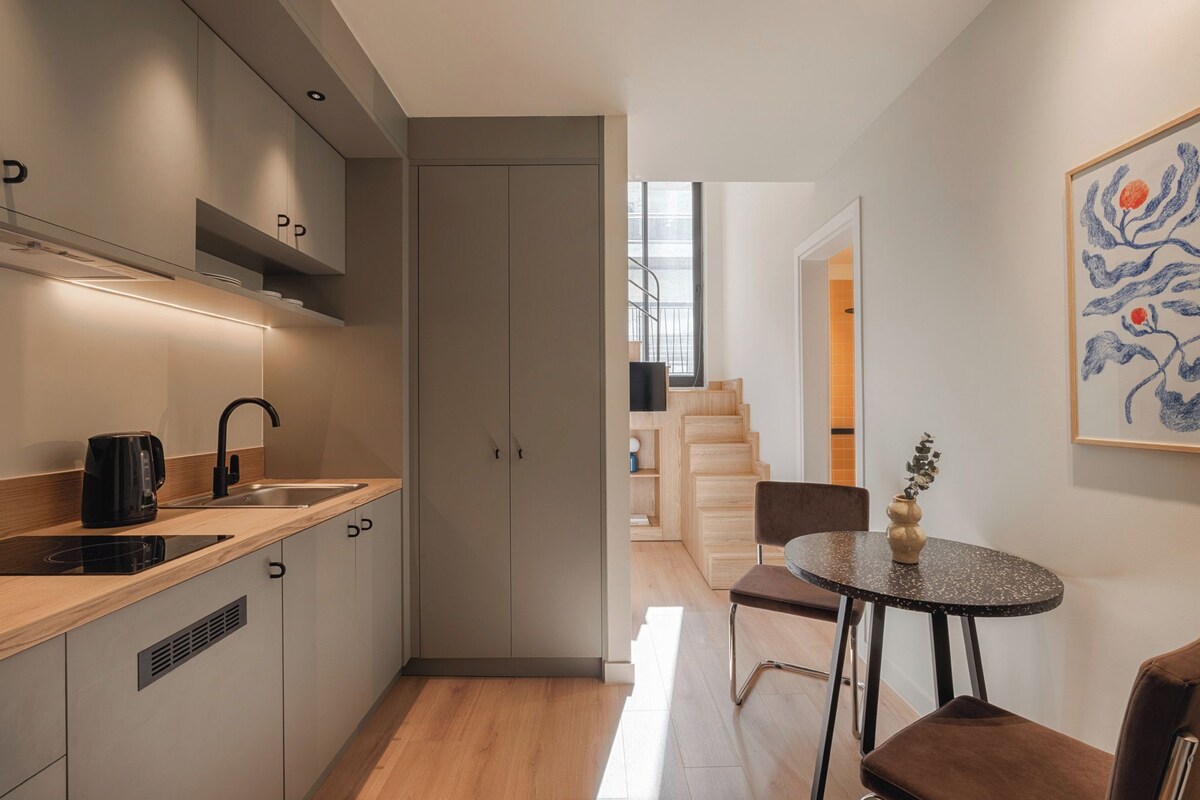 Una cocina moderna con horno empotrado, pileta y comedor con mesa y sillas.