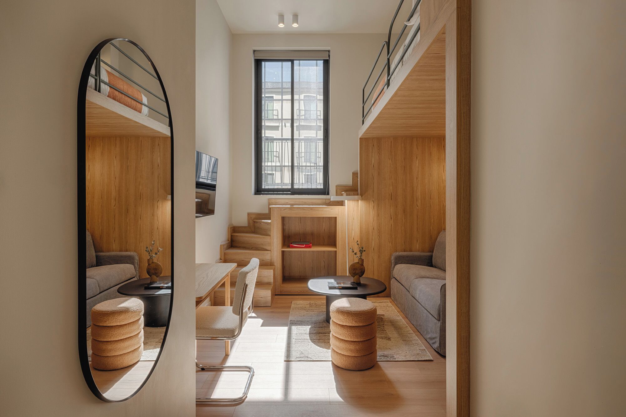 A compact living space with a mirrored wall, a staircase, a sofa, a coffee table, and a round ottoman.