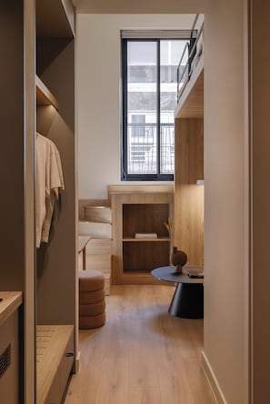 Una habitación compacta con armario empotrado, un pequeño rincón de descanso con mesa, y ventana con vistas al exterior.