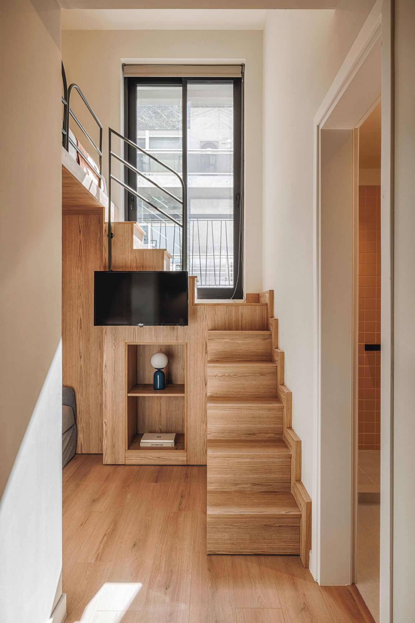 Una moderna scala con gradini in legno e ringhiera in metallo, che conduce a un balcone con vista sugli edifici.