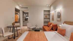 A hotel room with a bed, a sofa, a small table, a chair, a kitchenette, and a wardrobe. - Leon II by Zoia Living (Piraeus)