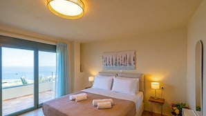 A hotel room with a large bed, two bedside lamps, a painting on the wall, and a view of the sea through a sliding door. - Sea Soul Luxury Villa with private swimming pool (Crete)