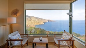 A room with a large window overlooking a coastal landscape, two wooden chairs, a small table, and a lamp. - Sea Soul Luxury Villa with private swimming pool (Crete)