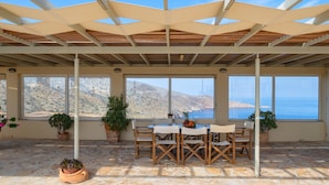 A covered outdoor seating area with stone flooring, wooden chairs, a table, and potted plants. - Sea Soul Luxury Villa with private swimming pool (Crete)