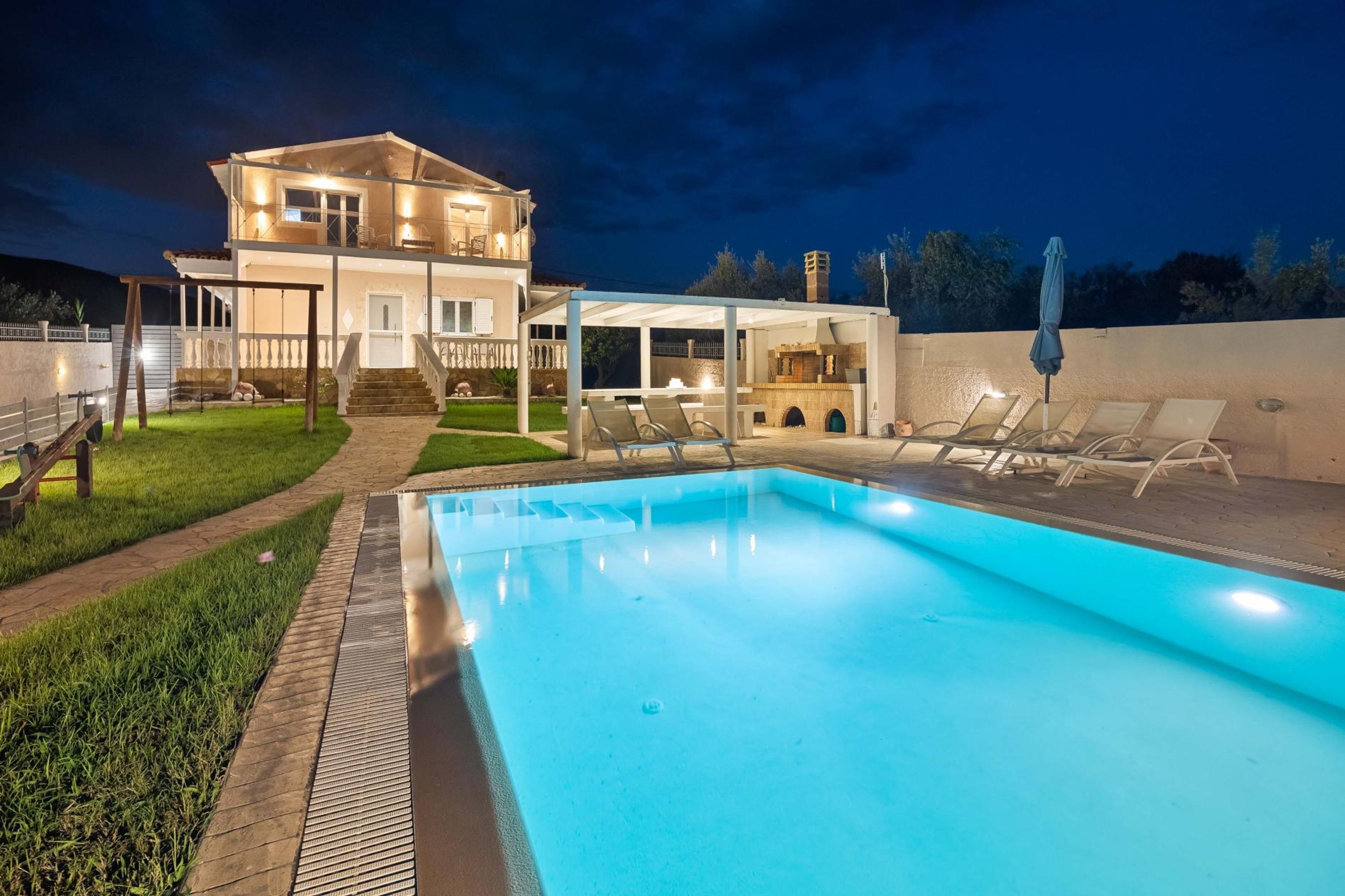 A modern two-story house with a swimming pool, outdoor seating, and a well-lit patio area.