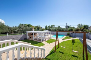 A backyard with a swimming pool, a wooden swing set, and a covered seating area. - Villa Anastasis in Crete (Crete)