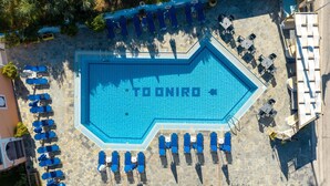 En bild tagen från luften som visar en swimmingpool där ordet ”TOONIRO” är skrivet på vattenytan. Runt poolen finns solstolar och bord.