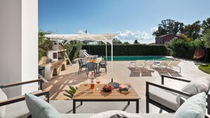 Een terras buiten met een zwembad, zitplaatsen en een pergola.