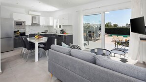 Een moderne keuken met witte kasten, een eettafel en een grijze bank.