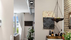 A modern kitchen with a hanging fruit basket, a chalkboard sign, and wine bottles on the counter.
