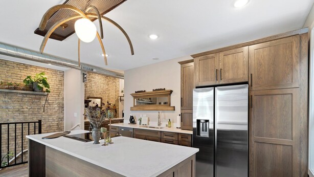 A modern kitchen with a large island, wooden cabinets, stainless steel appliances, and a brick accent wall.