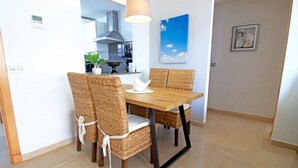A dining area with a wooden table and wicker chairs, a pendant light, a kitchen in the background, and a framed picture on the wall. - Castillo Bajo in Torrox (Torrox)