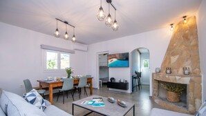 Una sala de estar moderna con sofá, mesa de comedor y sillas, chimenea de piedra y un televisor montado en la pared.