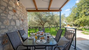 Un espacio para comer al aire libre con pared de piedra, barandilla metálica y vista a un paisaje verde.