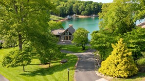 Une maison avec une allée menant à un lac, entourée d’arbres et dotée d’une pelouse bien entretenue.