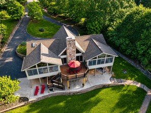 A two-story house with a stone chimney, a covered patio with red furniture, and a stone pathway leading to the entrance. - We have Water! Spacious home with Gentle Slope and Dock! (Moneta)