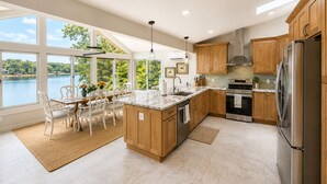 Une cuisine moderne dotée d’un grand îlot central, de meubles en bois, d’appareils électroménagers en acier inoxydable et offrant une vue sur un lac.