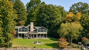 Une grande maison à plusieurs étages, dotée d’une cheminée en pierre, d’une terrasse et offrant une vue sur un lac.