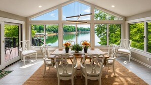 Un espace repas offrant une vue sur un lac, entouré de grandes fenêtres et de chaises blanches.