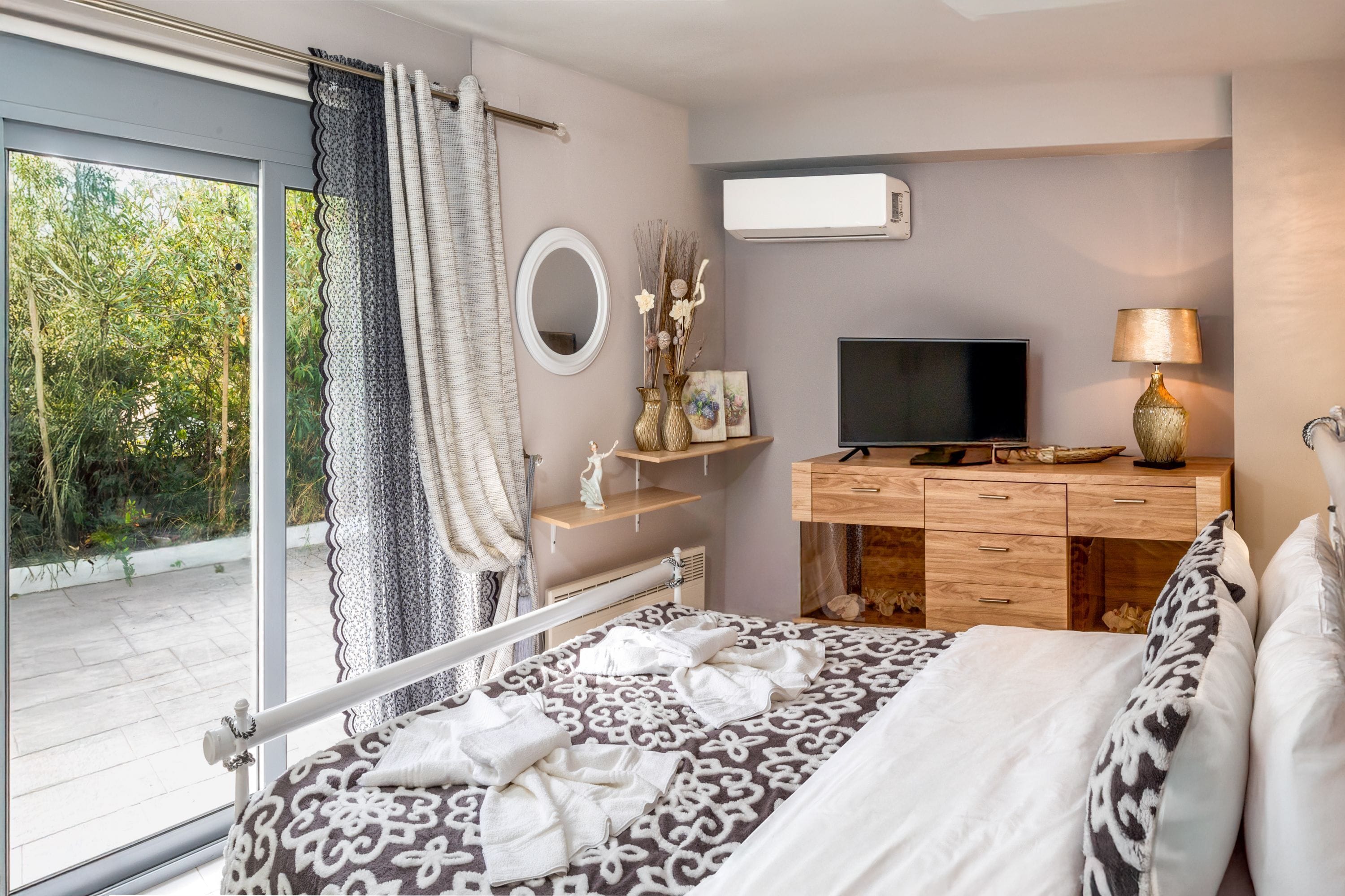 Een slaapkamer met een groot bed, een televisie, een dressoir en een raam met uitzicht op groen.