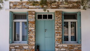 A building with a stone facade, a turquoise door, and two windows with shutters. - Aelios Cycladic house (Ormos Panormou)